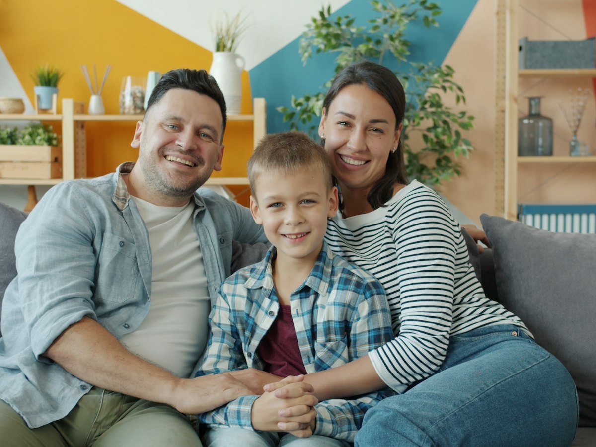 A family of three smiling together on their couch at home