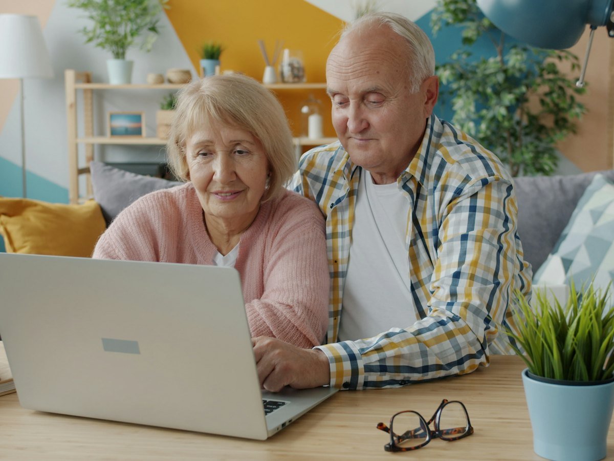 A couple smiling as they review their finances on a laptop at home